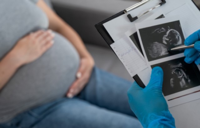 A pregnant woman holds her belly whilst a doctor examines ultrasound pictures of her baby