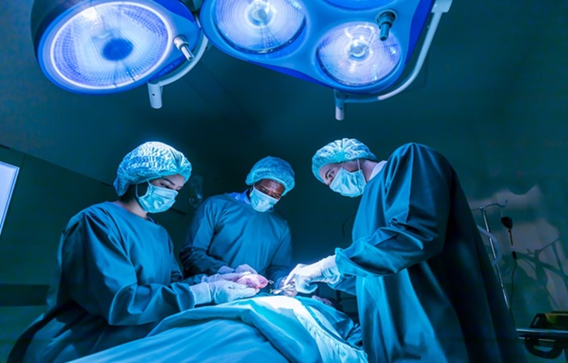 3 medical professionals with face masks and scrubs operate on a patient in an operating room