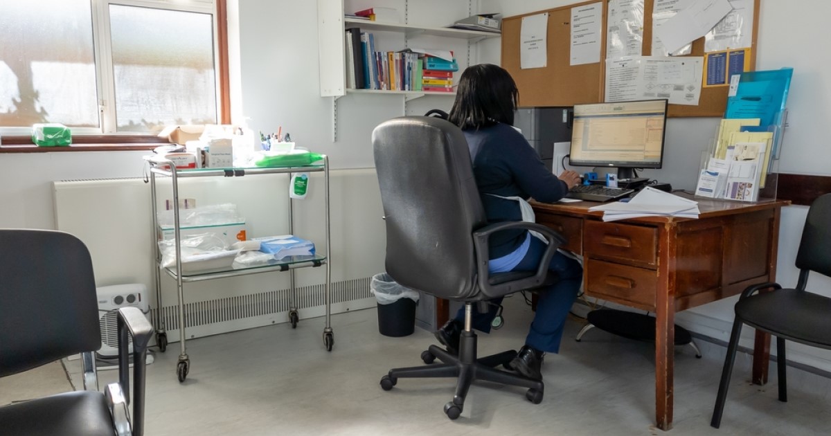 A GP works at a computer in their consultation room