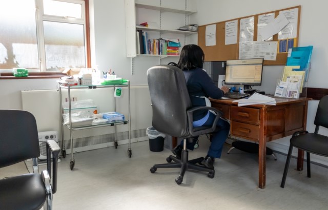 A GP works at a computer in their consultation room