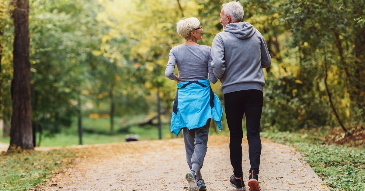 Photograph of an older couple wearing athletic wear walking along a path with trees either side.