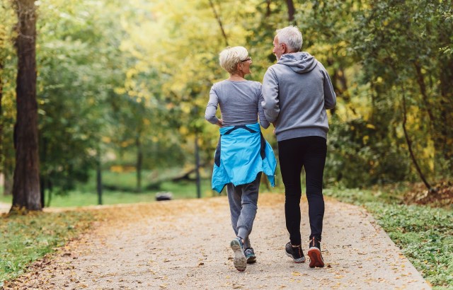 Photograph of an older couple with sportswear walking along a road with trees on each side.