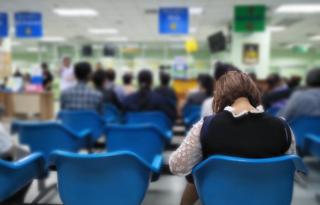 A woman sits with her back to us in a crowded hospital waiting room with her head down