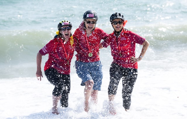 Three women in the surf at Brighton seaside wearing biking gear