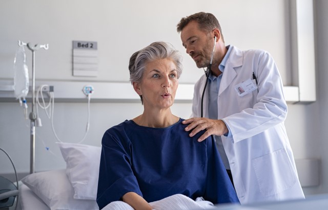 A doctor wearing a white coat holds a stethoscope to a woman's back 