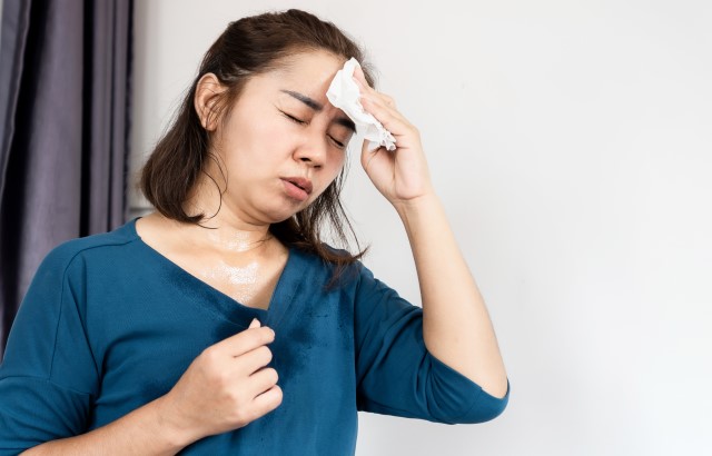 A young Asian woman wearing a blue top dabs her forehead with a white cloth