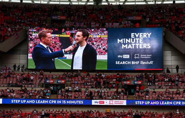 Presenter Simon Thomas interviewing footballer Tom Lockyer live on the big screen of Wembley