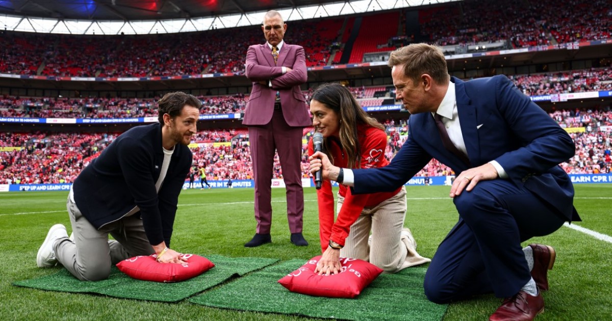 Footballer Tom Lockyer and the BHF's Lizzie Moscardini lead a CPR demo at Wembley Stadium with Vinnie Jones watching on.