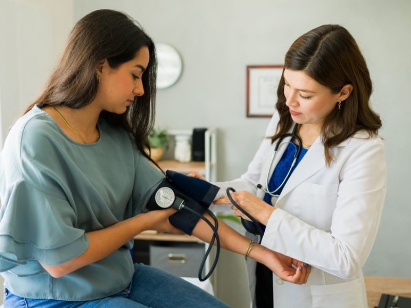A young woman has her blood pressure checked by a doctor