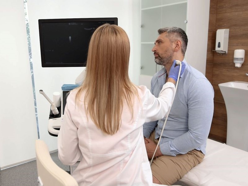 A female doctor scans a man's neck using an ultrasound device