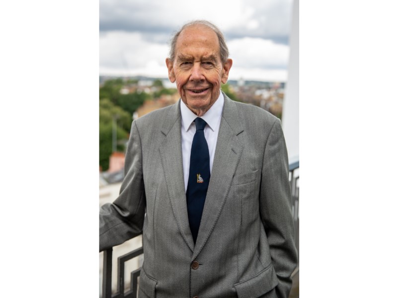 Photograph of Sir Terence English, smiling looking at the camera. He is wearing a grey suit, white shirt and black tie