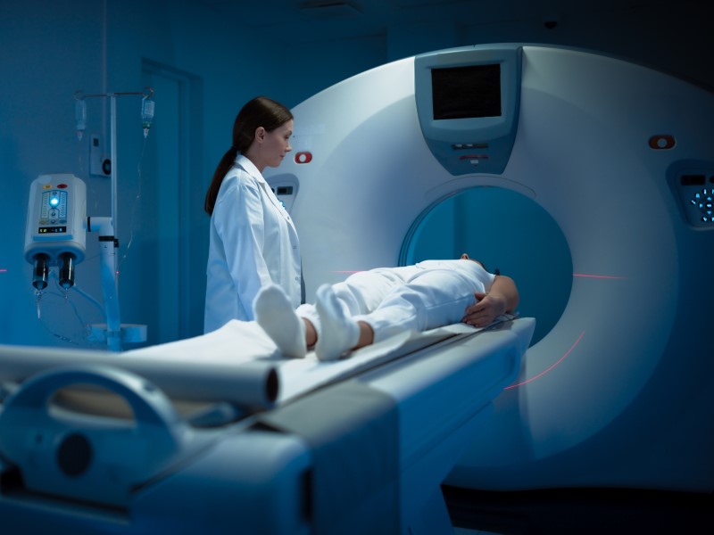 A patient lies on the bed in front of a scanner with a doctor stood next to them