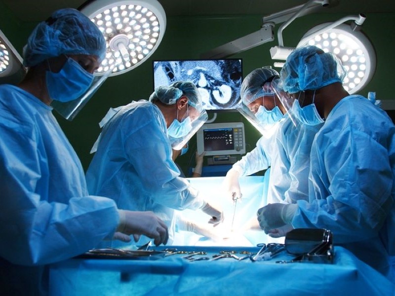 Four medical professionals dressed in blue scrubs stand over a patient and carry out heart surgery in an operating theatre