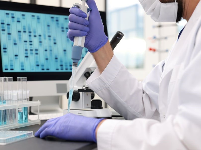 Scientist in a lab putting a blue liquid into a test tube in front of a computer