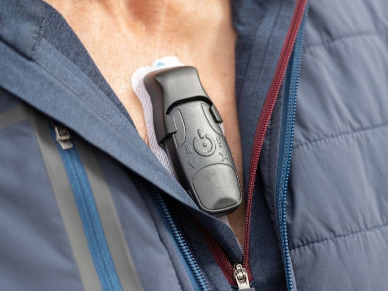 A small heart monitor, being worn on the chest with the quarter zip on a jumper undone to reveal it