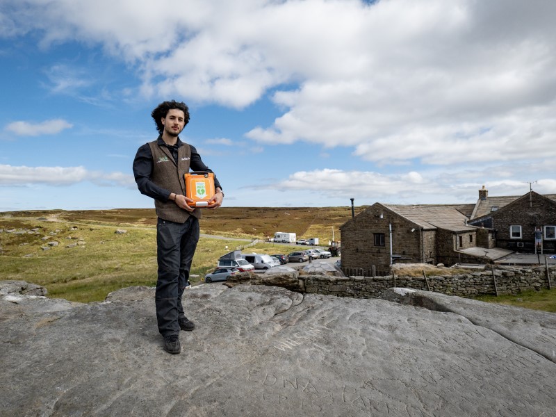 A tall young man stands on a rock outside the Tan Hill Inn, the UK's highest pub