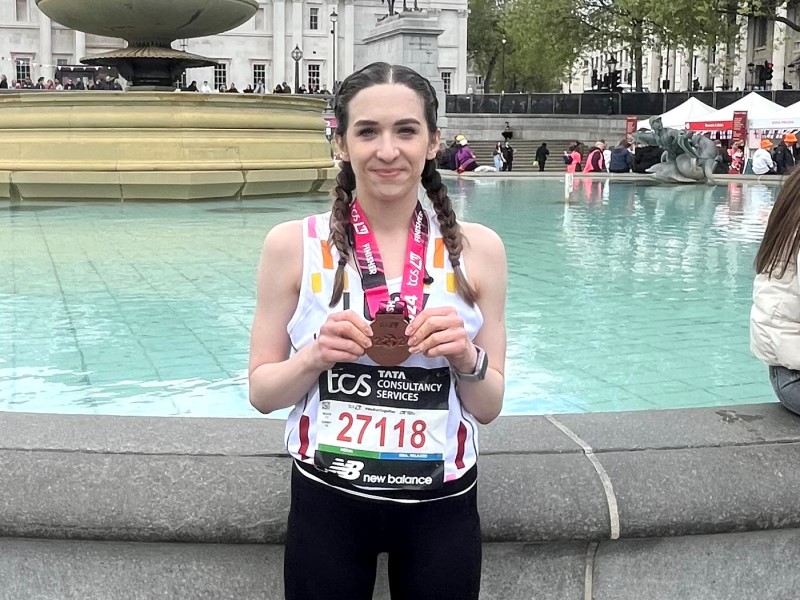 Lucy Shepherd after finishing the 2024 London Marathon, stood in front of a fountain showing off her medal