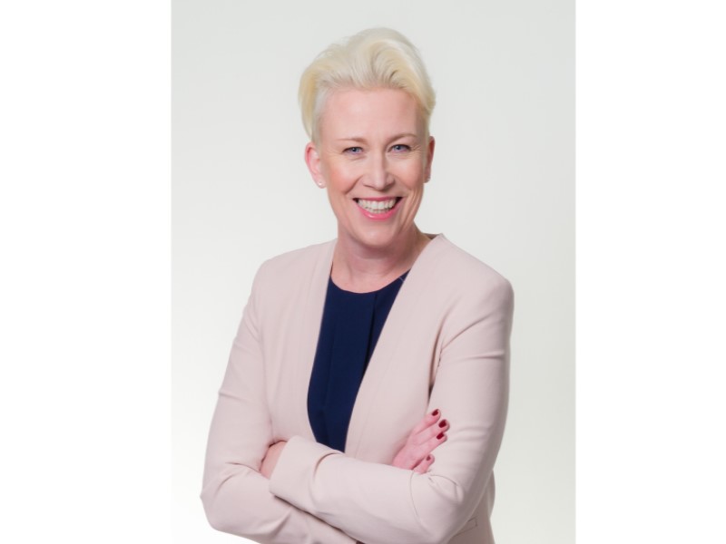 Allison Swaine-Hughes, wearing a pink blazer and blue top. Smiling at the camera with her arms folded