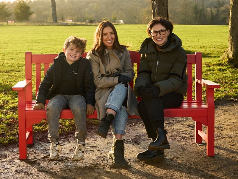 TV presenter Emma Willis sits on a BHF red bench with cardiovascular disease survivors Aimee and Leo Nicholls