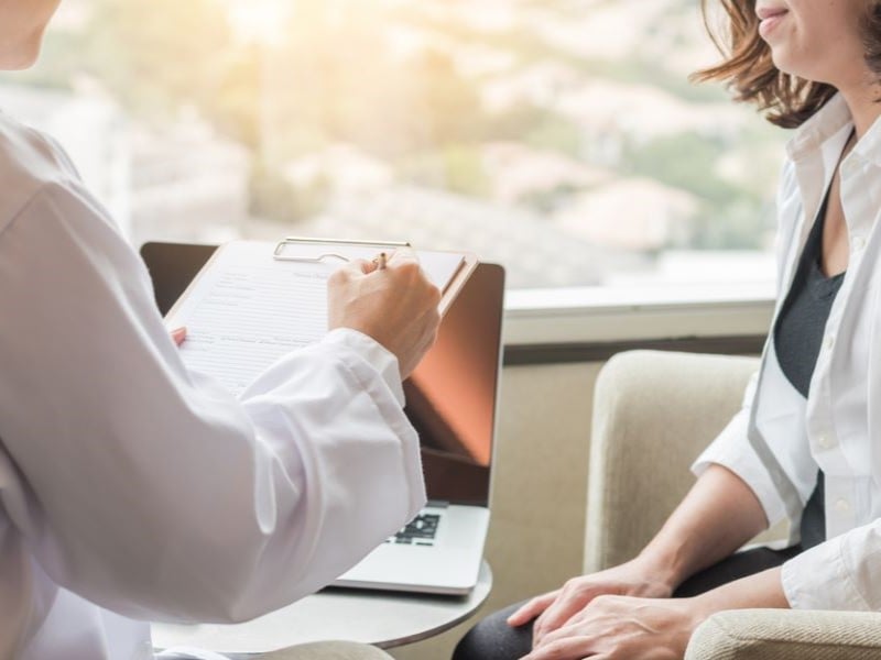 A doctor speaks with a woman and makes notes on a clipboard