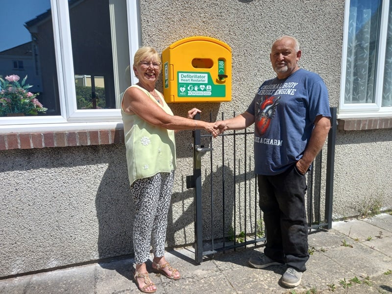 Two people standing beside a public access defibrillator mounted outside a building