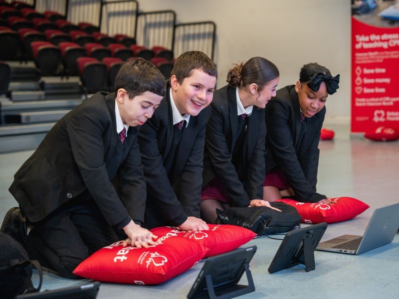 A row of young people learn CPR on British Heart Foundation-branded cushions