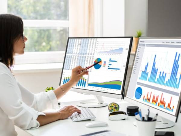 a young man sitting at a desk pointing at a pie chart on her computer screen