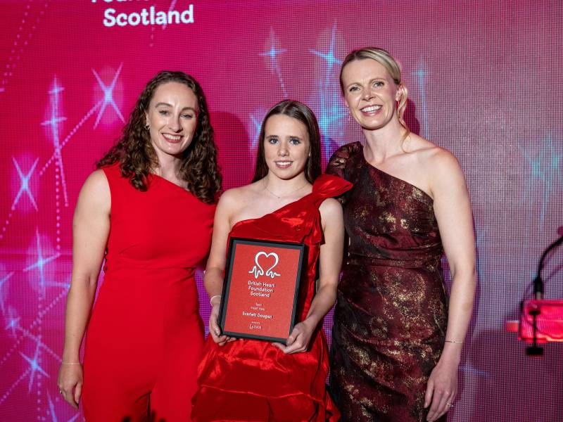 A young girl stands between two woman and holds a plaque