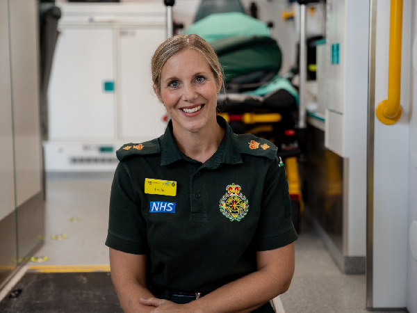 a female ambulance worker with blonde hair smiling and sitting inside an ambulance van