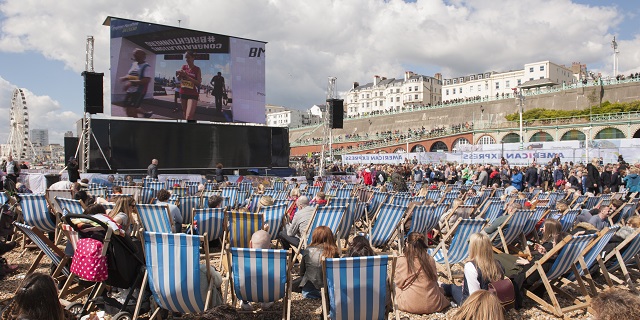 spectators on Brighton beach sitting on deck chairs watching runners finish the marathon